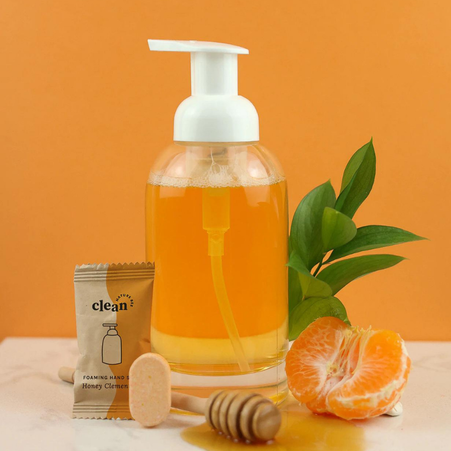 Glass, foaming hand soap dispenser containing orange Nature Bee hand soap.